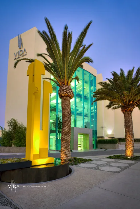 The glass atrium of VIDA Wellness & Beauty lit in the evening, the Recovery Boutique above the operating rooms.